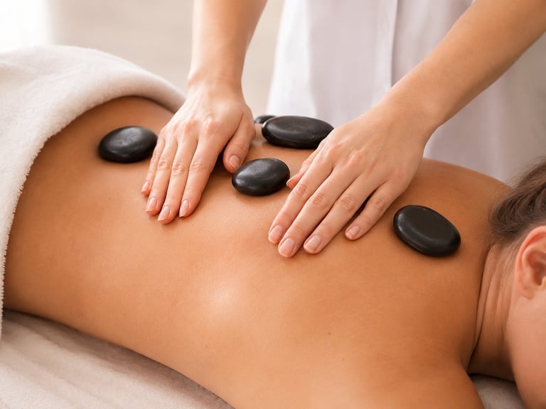 Therapist performing hot stone massage on clients back with black heated stones