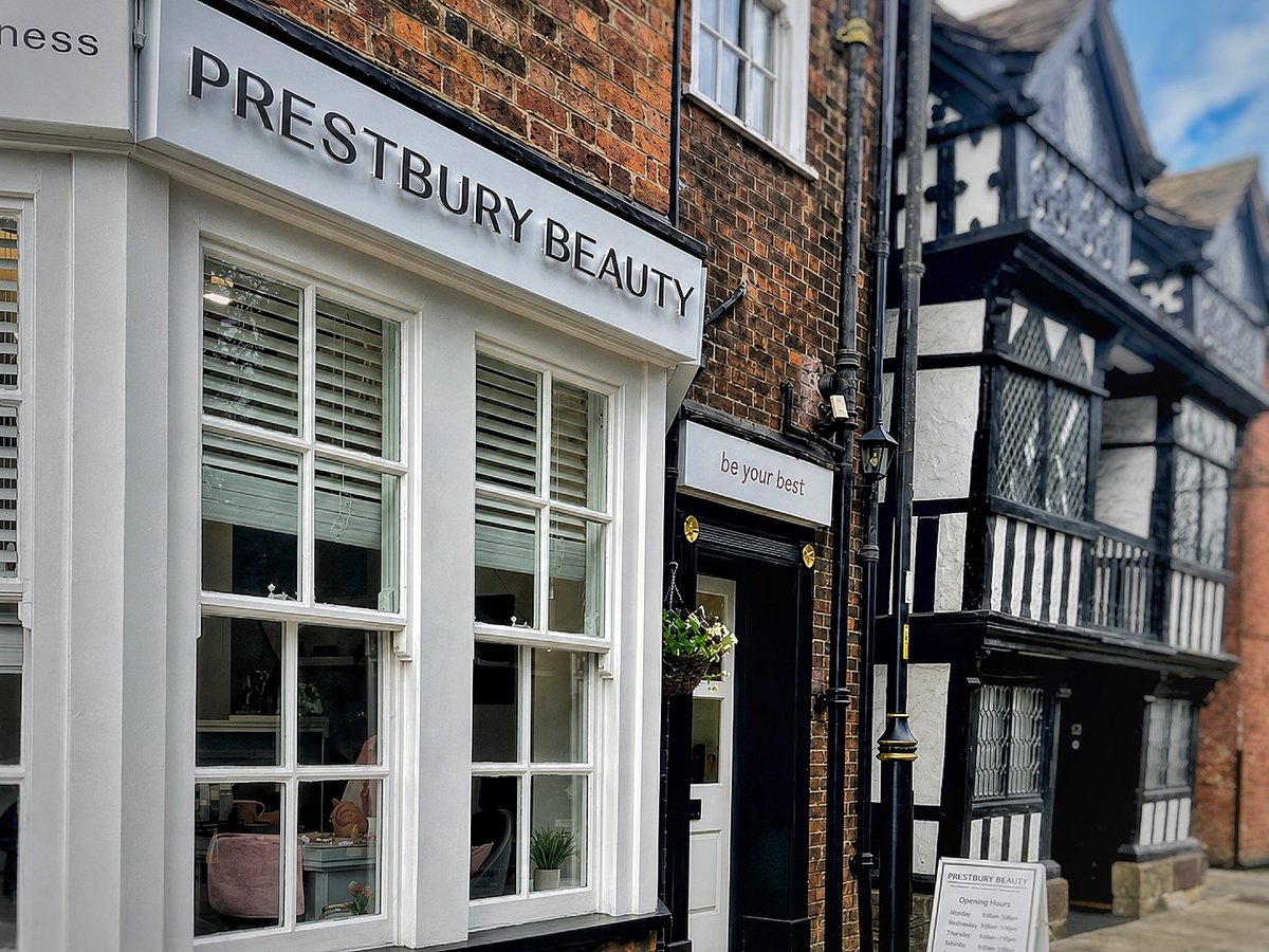 Prestbury Beauty storefront with white trim and large windows next to a traditional half-timbered building on a historic street