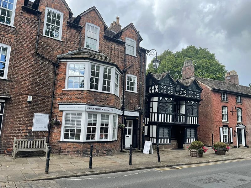 Historic brick buildings with a Tudor-style timber-framed structure in the center, featuring distinctive white and black patterns, lining a street