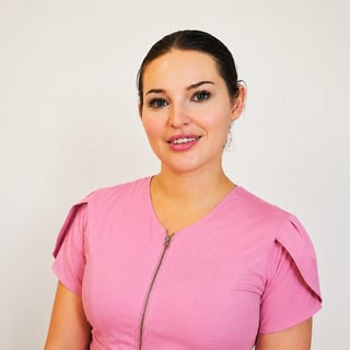Professional headshot of a woman with dark hair wearing a pink scrubs top against a light gray background