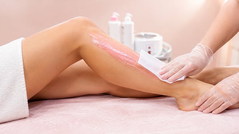 Esthetician applying pink wax to womans leg during hair removal treatment in spa setting